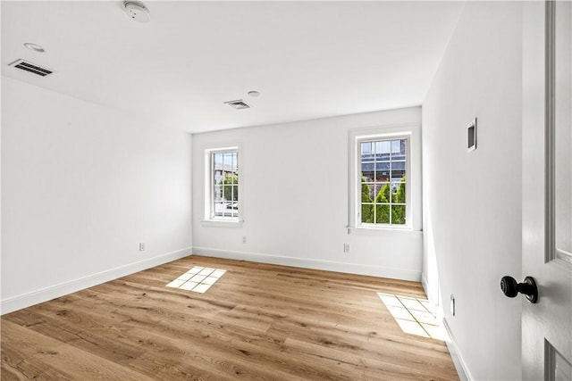 empty room featuring a healthy amount of sunlight, visible vents, and light wood-type flooring