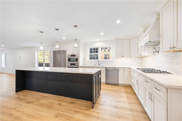 kitchen with a sink, a center island, stainless steel appliances, light wood-style floors, and decorative backsplash
