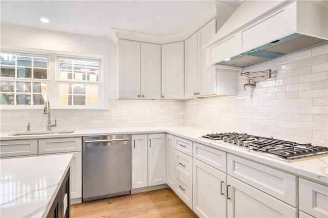 kitchen featuring a sink, stainless steel appliances, custom range hood, white cabinets, and light wood-style floors