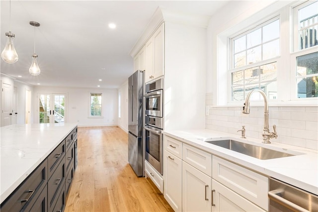 kitchen featuring a sink, white cabinetry, stainless steel appliances, light wood-style floors, and decorative backsplash