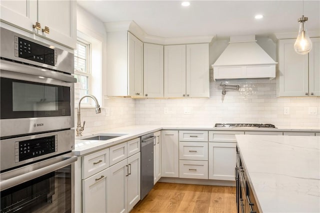 kitchen featuring premium range hood, light wood finished floors, stainless steel appliances, a sink, and white cabinetry