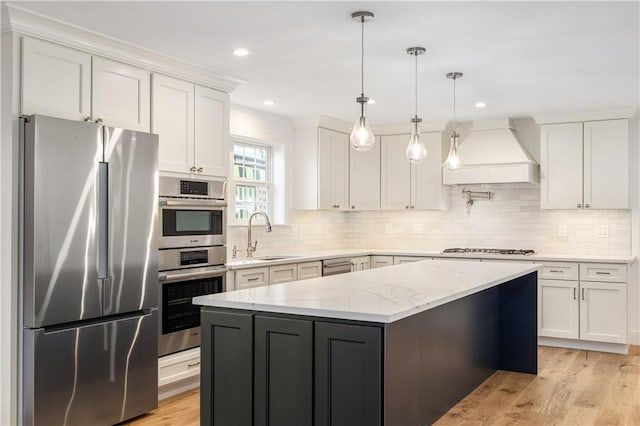 kitchen featuring premium range hood, a sink, a kitchen island, appliances with stainless steel finishes, and white cabinets