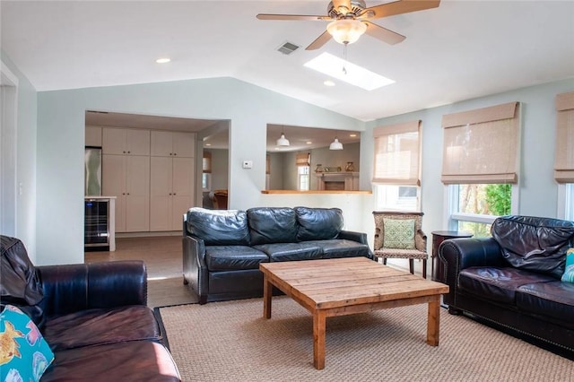 living area featuring beverage cooler, vaulted ceiling with skylight, a ceiling fan, and visible vents