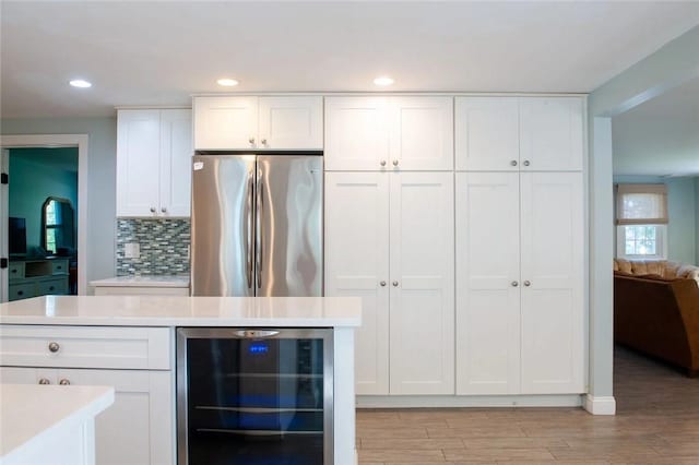 kitchen with backsplash, wine cooler, light countertops, freestanding refrigerator, and white cabinetry