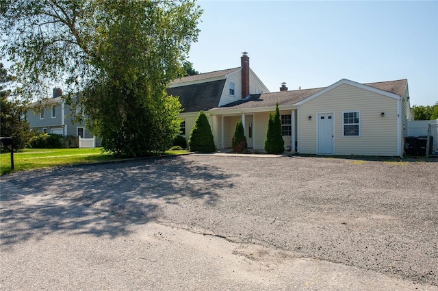 view of front of property featuring roof with shingles, gravel driveway, and a chimney