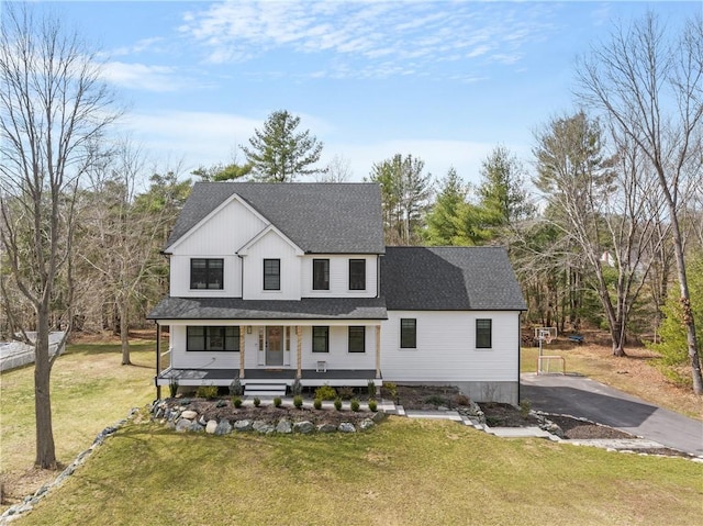 modern farmhouse style home with aphalt driveway, covered porch, a front lawn, and roof with shingles