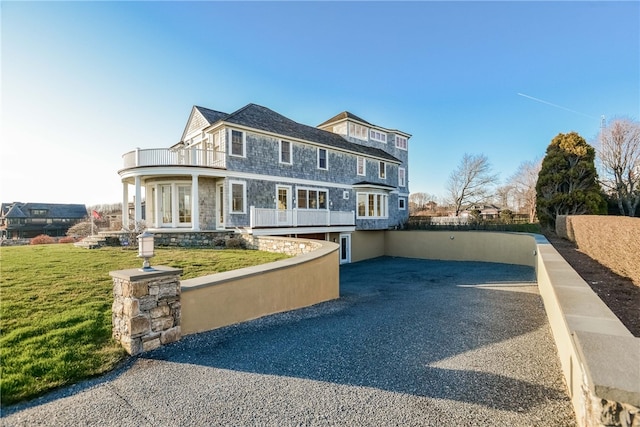 shingle-style home featuring fence, a front yard, a balcony, and french doors