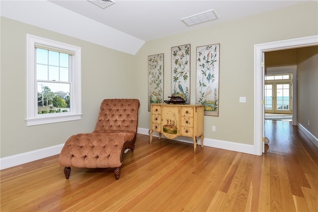living area featuring vaulted ceiling, light wood-style flooring, baseboards, and visible vents