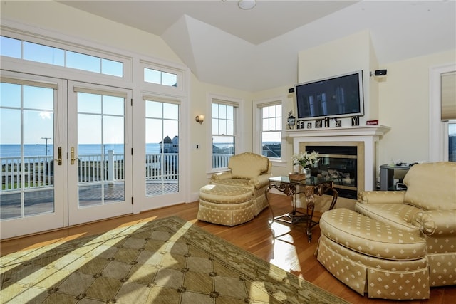 living area featuring french doors, a glass covered fireplace, wood finished floors, and lofted ceiling