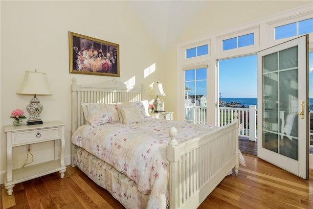 bedroom featuring a water view, access to exterior, wood finished floors, and lofted ceiling