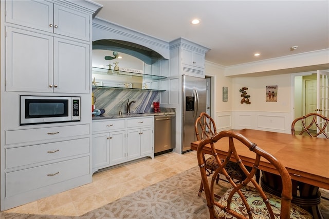 kitchen featuring ornamental molding, a wainscoted wall, a sink, stainless steel appliances, and backsplash