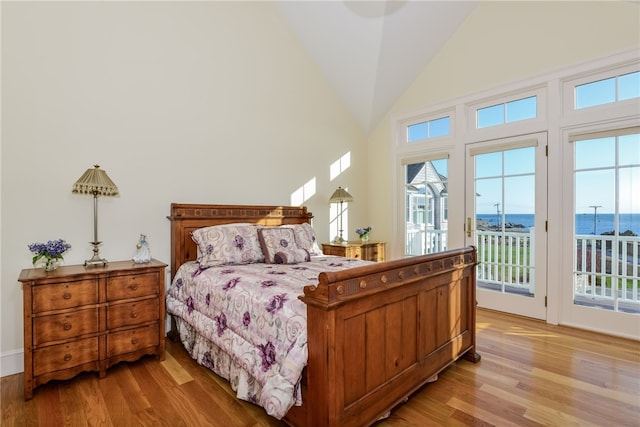 bedroom with access to outside, light wood finished floors, lofted ceiling, and a water view