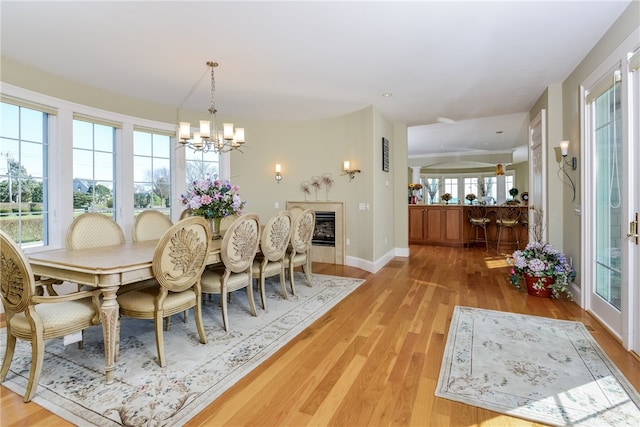 dining space with a chandelier, a glass covered fireplace, light wood-style flooring, and baseboards
