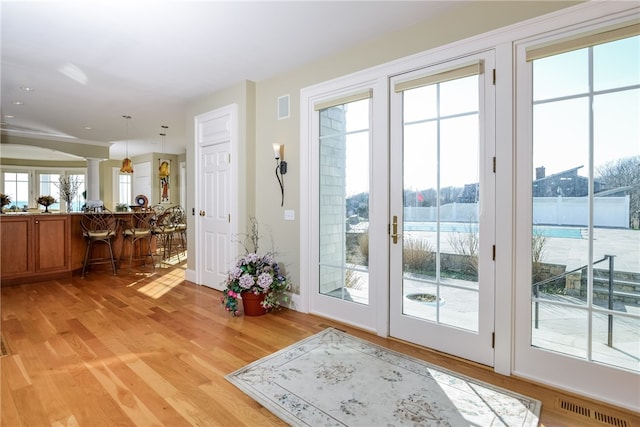 entryway with decorative columns, light wood finished floors, and visible vents