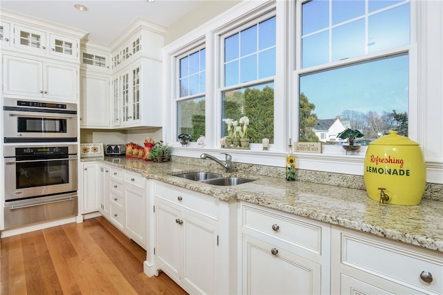 kitchen featuring a warming drawer, light wood-style floors, a healthy amount of sunlight, double oven, and a sink