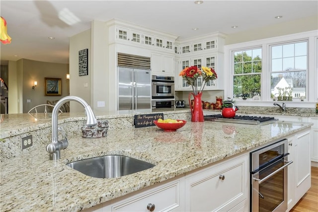 kitchen featuring glass insert cabinets, light stone countertops, white cabinetry, a sink, and stainless steel appliances