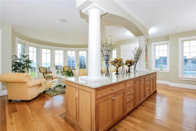 kitchen with visible vents, open floor plan, ornate columns, light wood-style flooring, and light stone counters