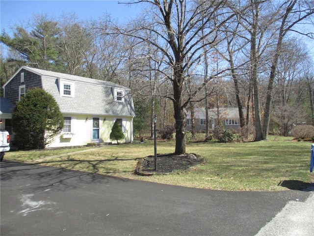 view of front of property with a gambrel roof, roof with shingles, and a front yard