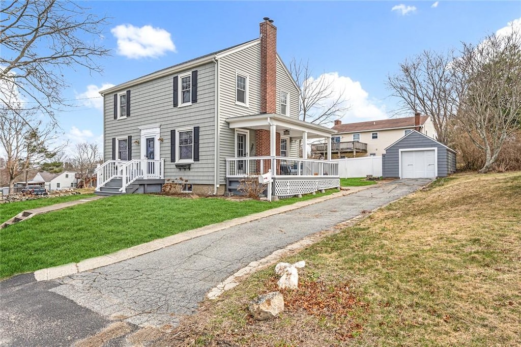 view of front of property featuring driveway, covered porch, a chimney, an outbuilding, and a front lawn