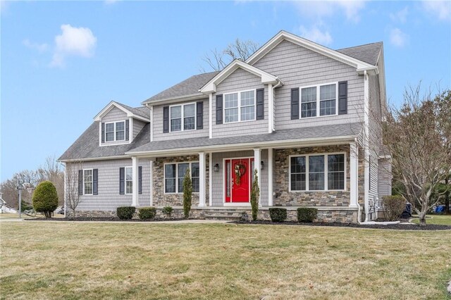 view of front of house featuring stone siding, covered porch, a front lawn, and a shingled roof