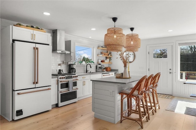 kitchen with wall chimney range hood, a healthy amount of sunlight, light wood finished floors, and high end appliances