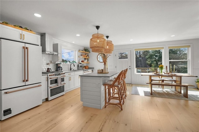 kitchen featuring a center island, white cabinetry, light wood-type flooring, premium appliances, and wall chimney exhaust hood