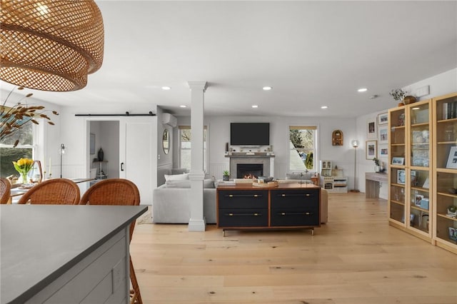 living room with recessed lighting, a warm lit fireplace, a barn door, decorative columns, and light wood-type flooring