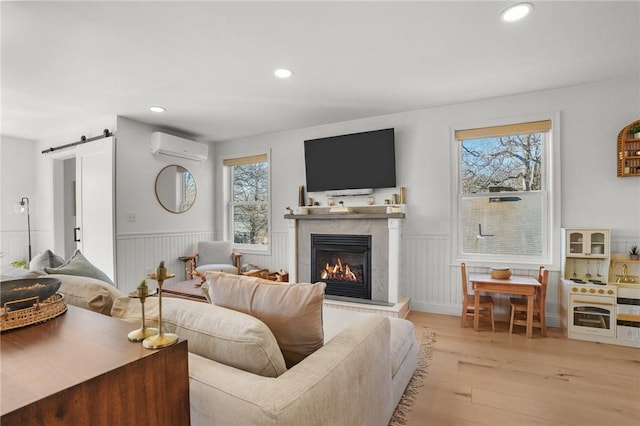 living area with a barn door, wood finished floors, an AC wall unit, and wainscoting