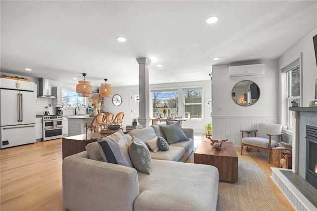 living room with a warm lit fireplace, plenty of natural light, an AC wall unit, and ornate columns