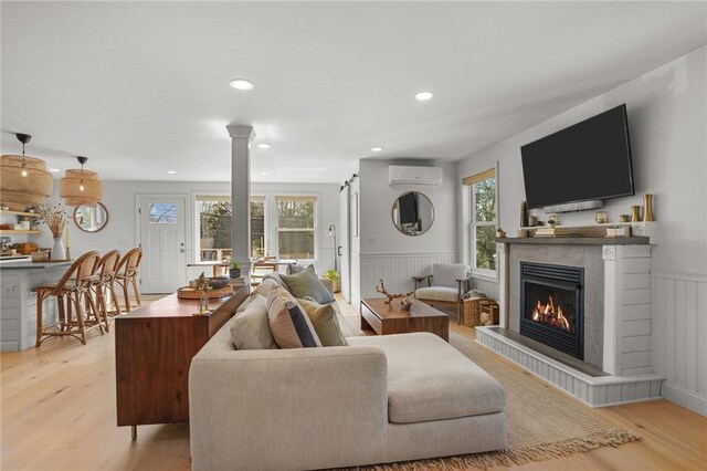 living room with an AC wall unit, wainscoting, light wood-type flooring, a tiled fireplace, and ornate columns