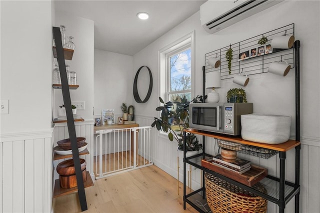 interior space featuring wainscoting, stainless steel microwave, a wall mounted air conditioner, and light wood-style flooring