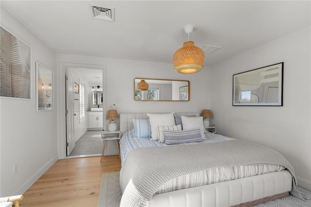 bedroom with ensuite bath, wood finished floors, visible vents, and baseboards