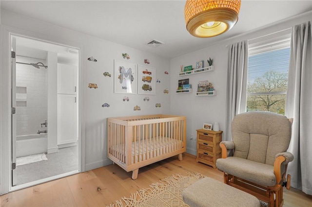 bedroom with visible vents, baseboards, wood finished floors, and a nursery area