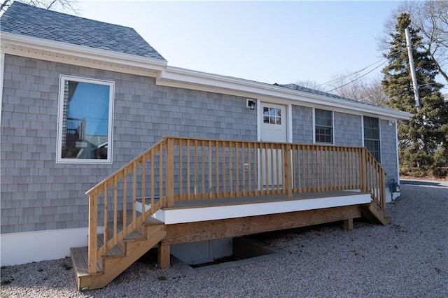 entrance to property featuring a shingled roof and a wooden deck