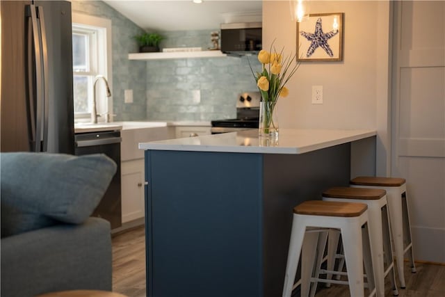 kitchen featuring decorative backsplash, a breakfast bar, stainless steel appliances, open shelves, and a peninsula