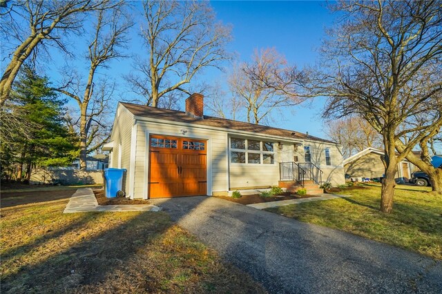 ranch-style home featuring driveway, an attached garage, a chimney, and a front yard