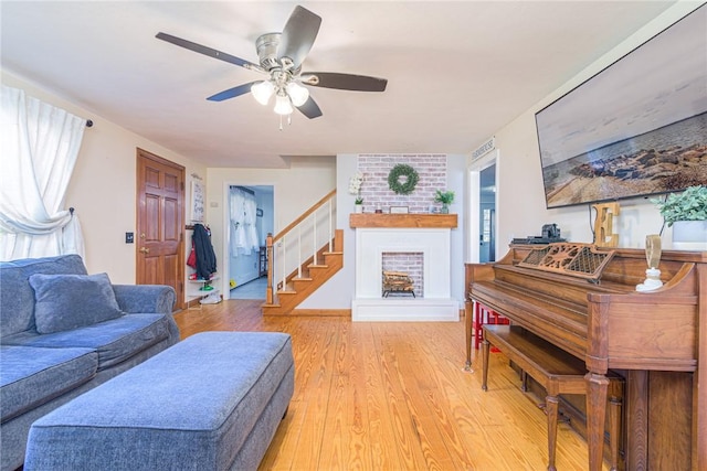 living area with stairway, a fireplace, a ceiling fan, and light wood-type flooring
