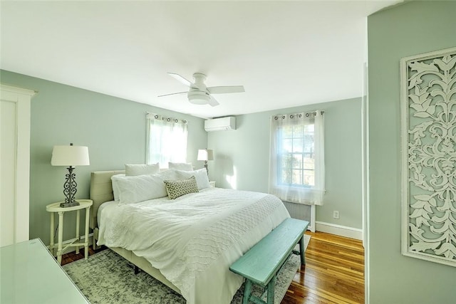 bedroom featuring a wall mounted air conditioner, baseboards, wood finished floors, and a ceiling fan