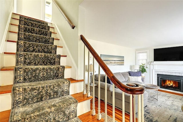 stairway featuring a warm lit fireplace and wood finished floors
