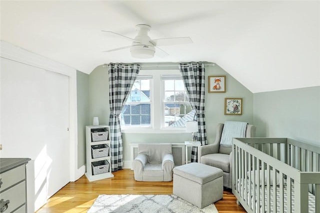 bedroom with ceiling fan, a nursery area, vaulted ceiling, and light wood-type flooring