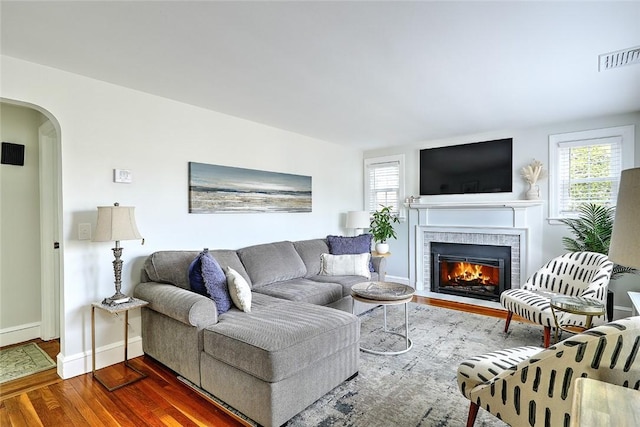 living room featuring a fireplace with flush hearth, dark wood-style flooring, visible vents, baseboards, and arched walkways