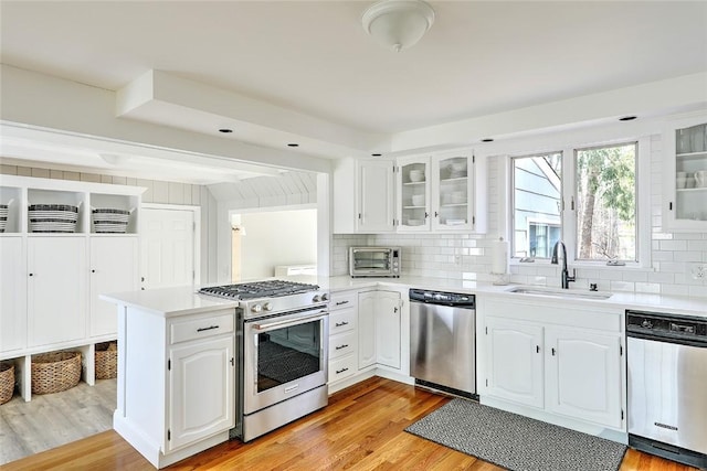 kitchen with light countertops, a peninsula, light wood finished floors, stainless steel appliances, and a sink