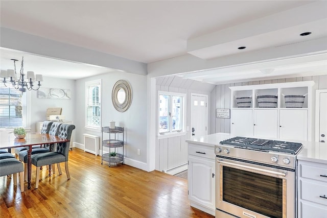 kitchen featuring a baseboard heating unit, gas range, a chandelier, light wood-style floors, and white cabinets