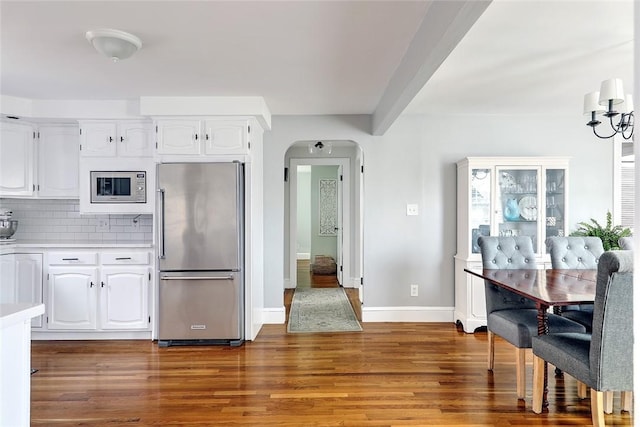 kitchen featuring light countertops, wood finished floors, appliances with stainless steel finishes, arched walkways, and decorative backsplash