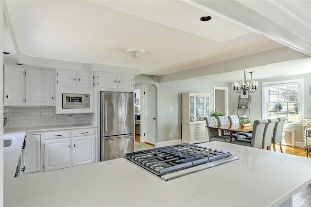 kitchen with light countertops, a chandelier, tasteful backsplash, stainless steel appliances, and white cabinets