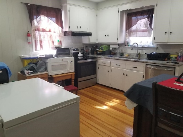 kitchen with white cabinets, under cabinet range hood, a sink, light wood-type flooring, and appliances with stainless steel finishes