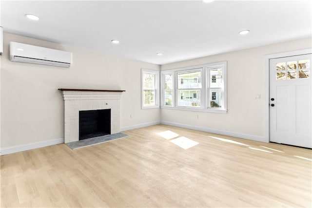 unfurnished living room with baseboards, a wall mounted AC, light wood-style floors, and a brick fireplace