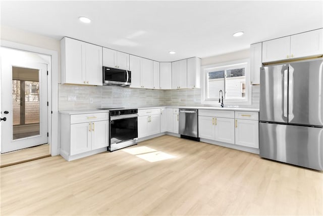 kitchen with decorative backsplash, light countertops, stainless steel appliances, white cabinetry, and light wood-type flooring