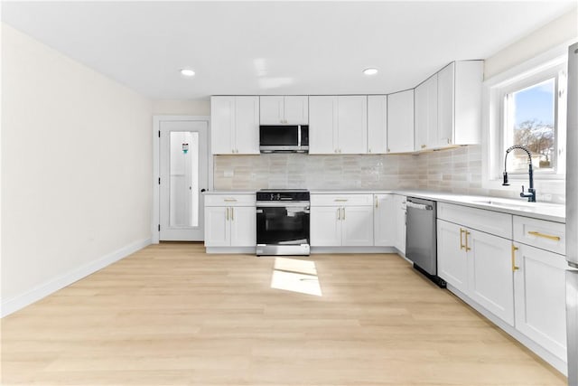 kitchen with decorative backsplash, white cabinets, light countertops, appliances with stainless steel finishes, and a sink