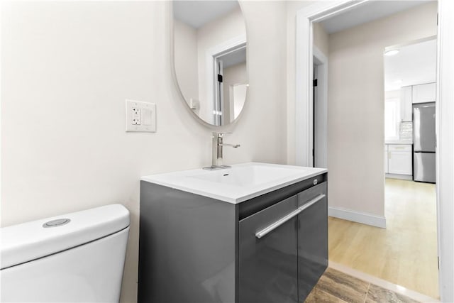 half bath featuring vanity, toilet, baseboards, backsplash, and wood finished floors